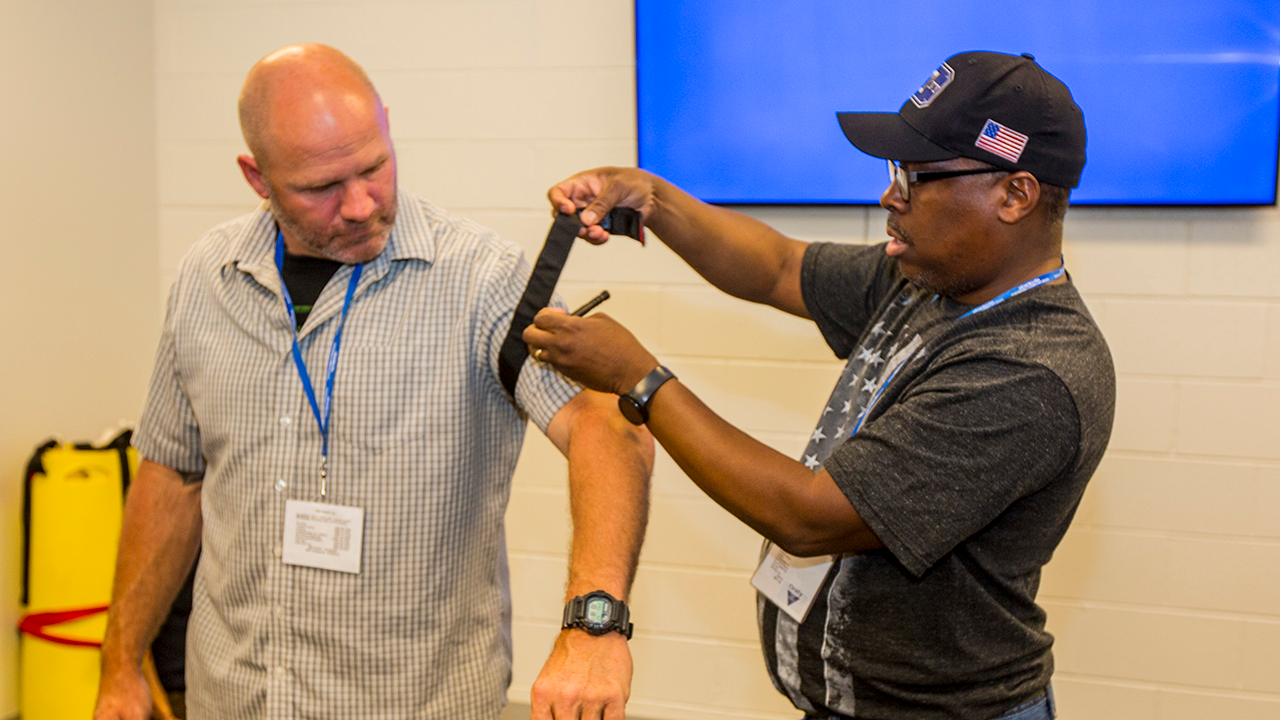 Instructor-in-training Winslow Harrison (right), an emergency medical technician, applies a tourniquet to the arm of a fellow student during the Instructor Training Course.