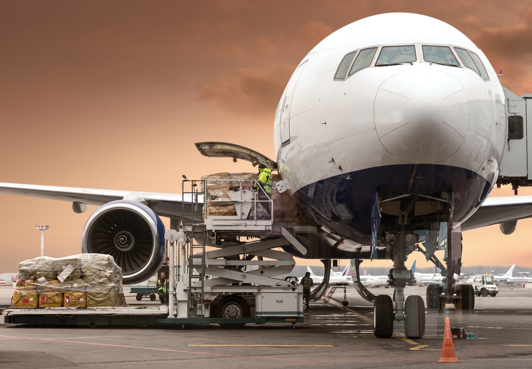 Image of a commercial airliner. On the left side of the plane a hatch is open and airport personel are operating a lift and loading bulk materials into the plane.