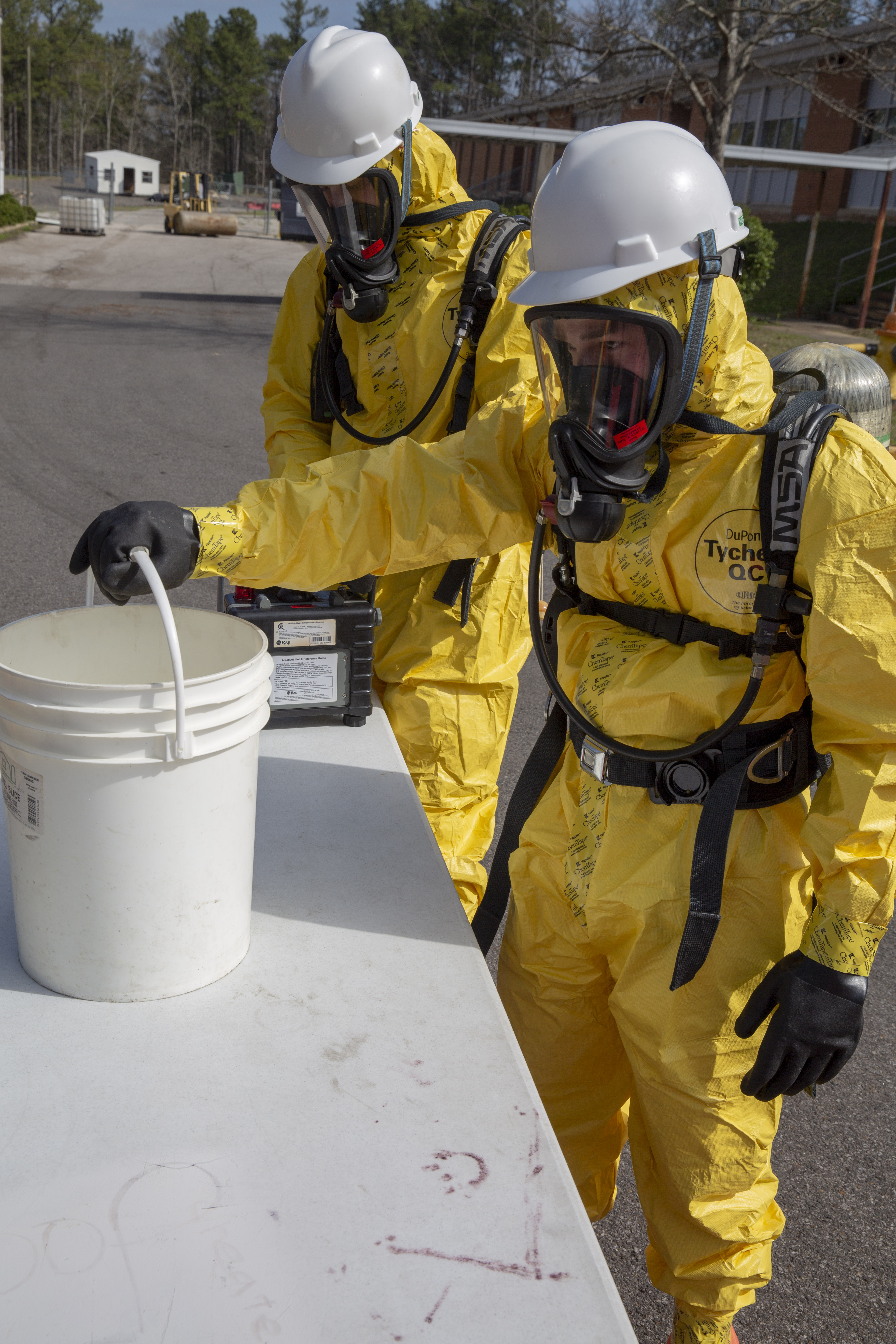 Two first responders in yellow Tyvek suits with white hard hats, wearing resperators.  This photo is to demonstrate precautions that responders take when responding to hazardous CBRNE situations.