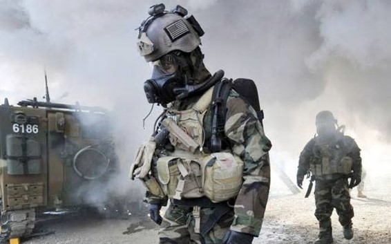 Photo of overturned vehicle with two soldiers in CBRN gear with "agent" smoke coming out of the overturned vehice.